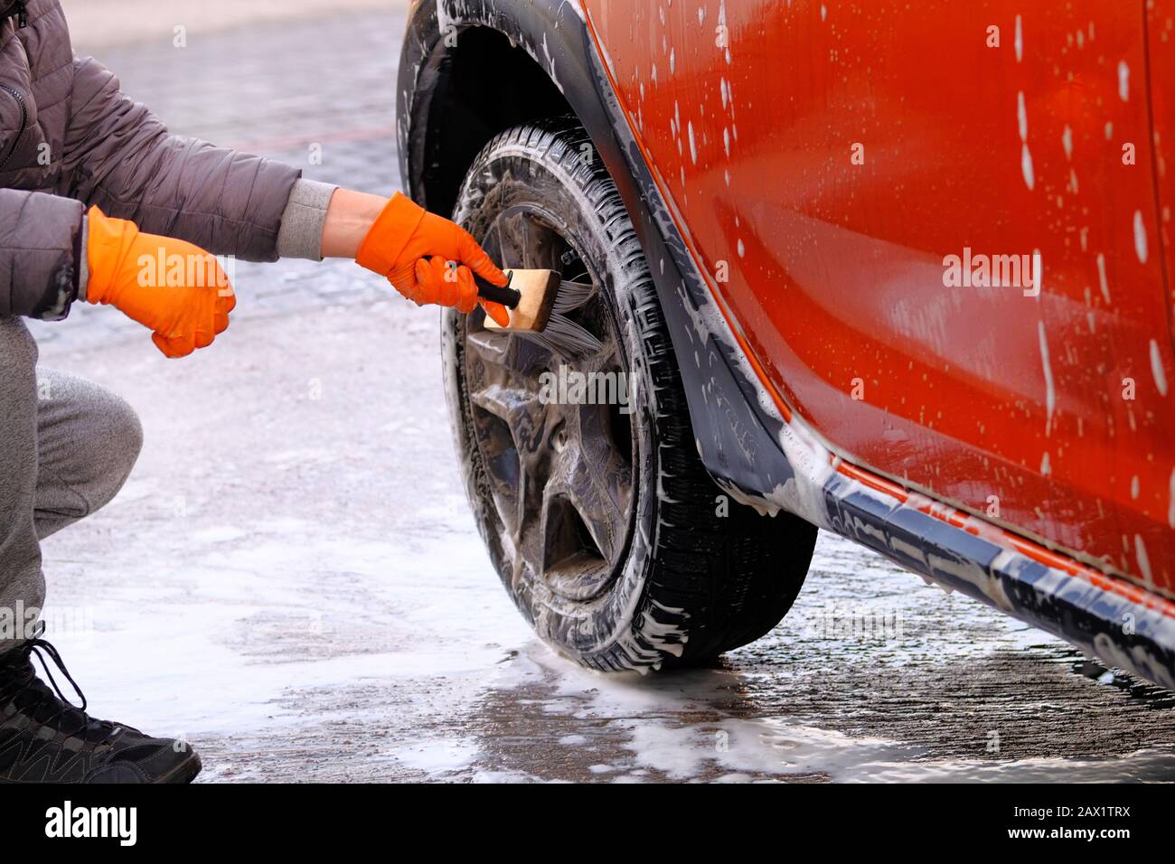 Pulizia con sapone in caso di autolavaggio self-service. Uomo in gomma  guanti lava ruota nera della sua auto arancione con spazzola. L'acqua  saponata si esaurisce Foto stock - Alamy