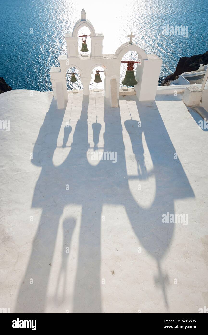 Luminoso sole mediterraneo che splende dietro il classico contorno di un campanile imbiancato nel villaggio collinare di Oia, Santorini, Grecia Foto Stock