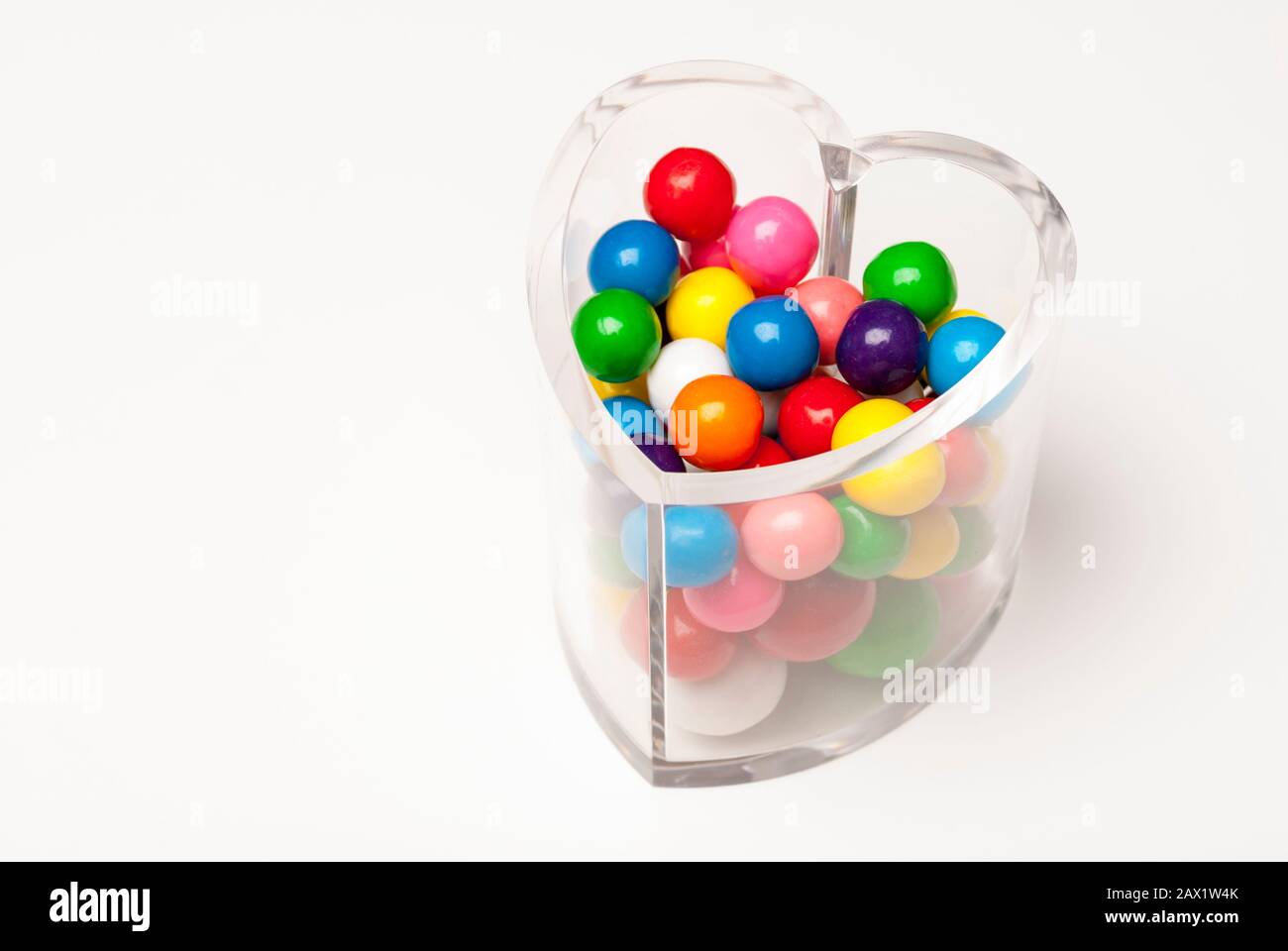 Vaso di caramelle chiaro a forma di cuore pieno di caramelle lucide e colorate gumball San Valentino su sfondo bianco Foto Stock