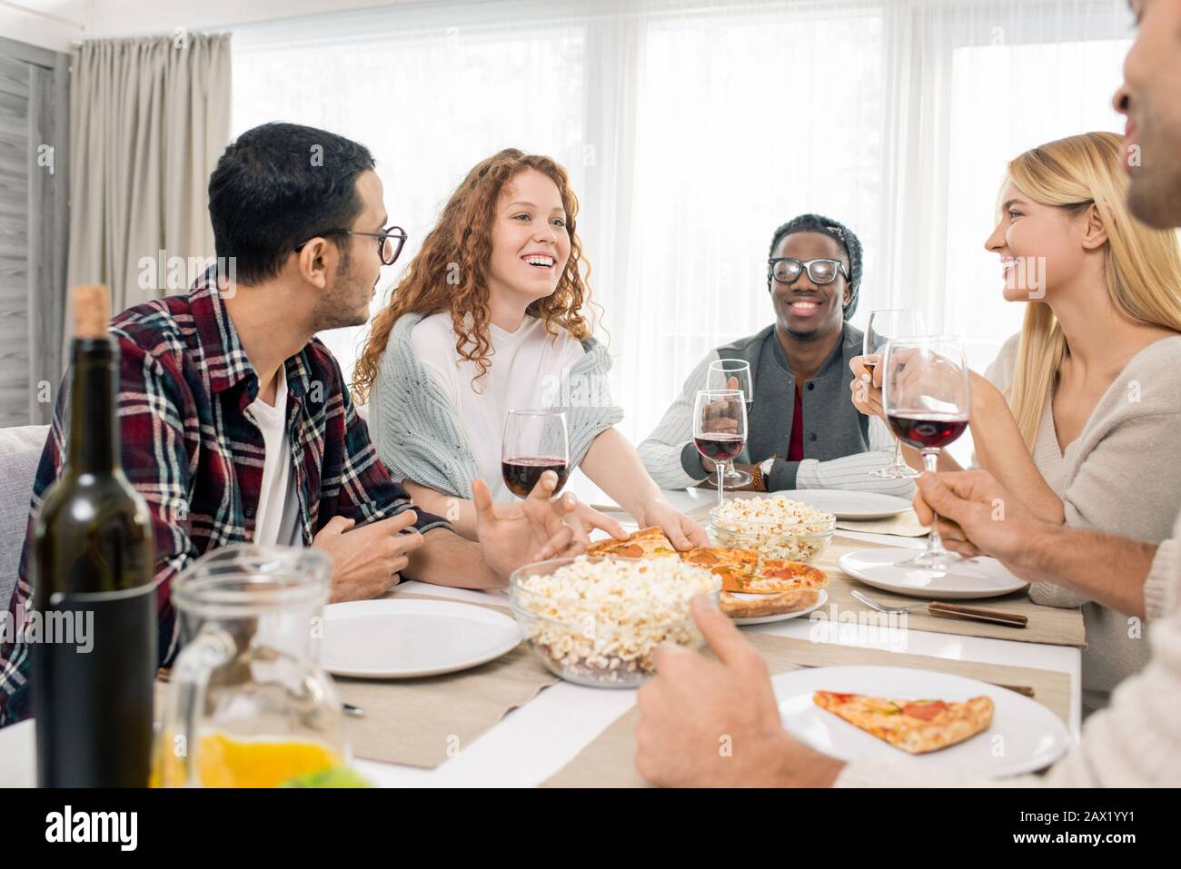 Gruppo multietnico di cinque amici che si rilassano al tavolo della cena insieme durante il fine settimana, scatto orizzontale Foto Stock
