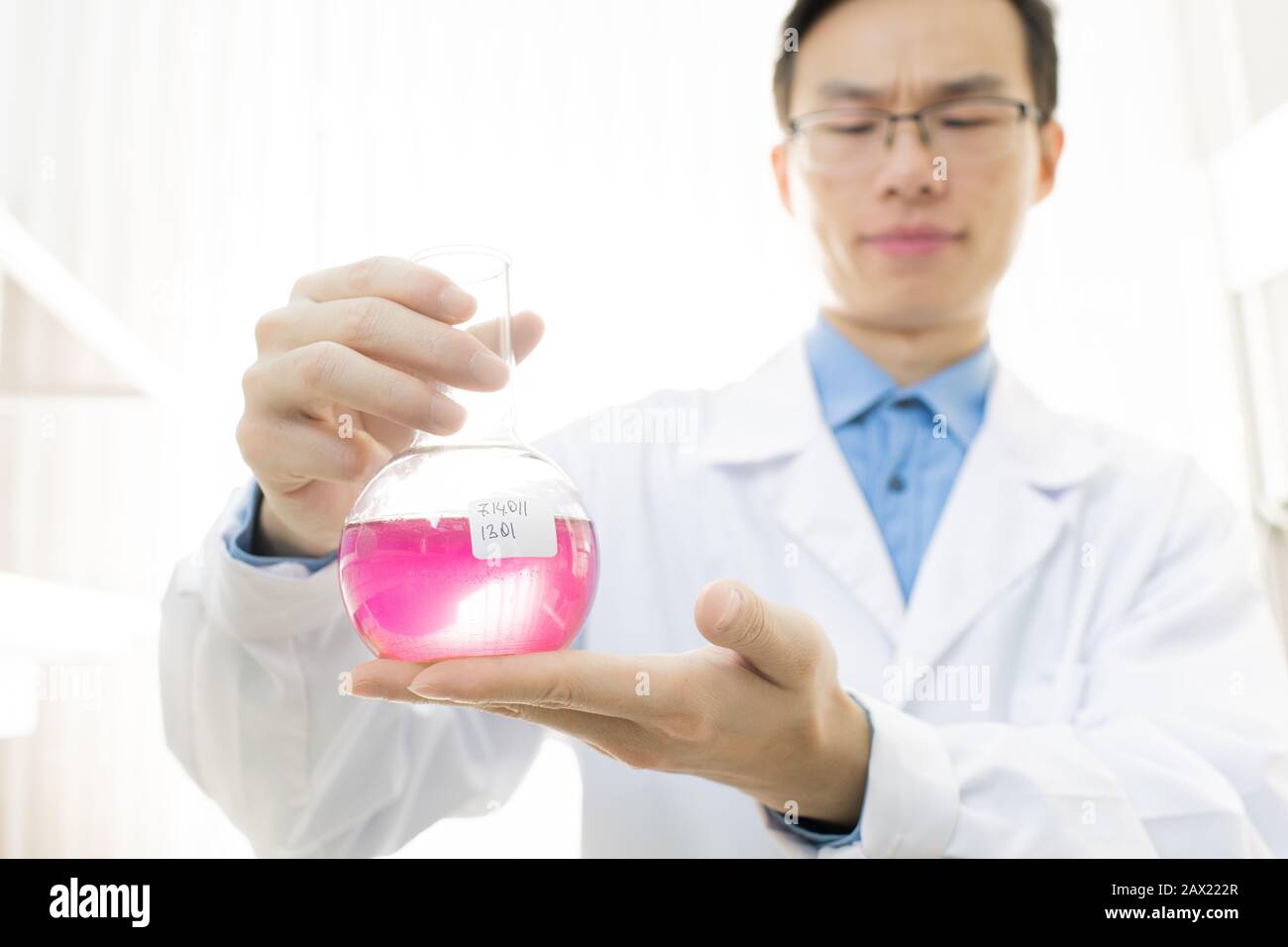 Ritratto orizzontale di giovani scienziati medici che indossano cappotto bianco e matraccio porta occhiali con liquido rosa Foto Stock