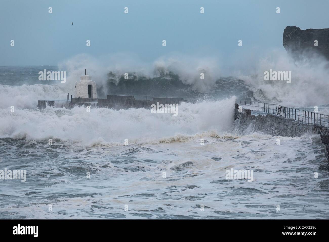 La tempesta Ciara batta la costa della Cornovaglia con onde giganti alte quanto le scogliere circostanti che si infrangono contro il frangiflutti Foto Stock