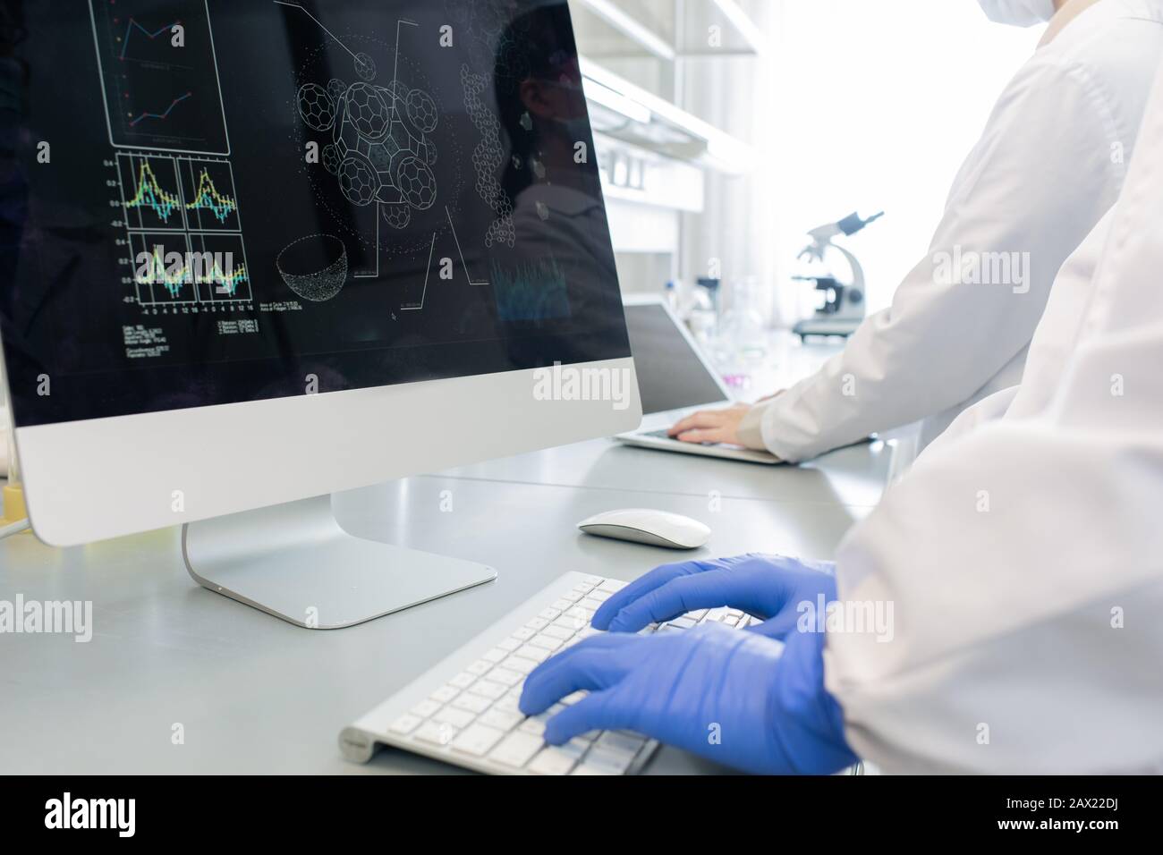 Scatto orizzontale di due scienziati irriconoscibili che indossano guanti di camice bianco che lavorano in laboratorio utilizzando computer moderni Foto Stock