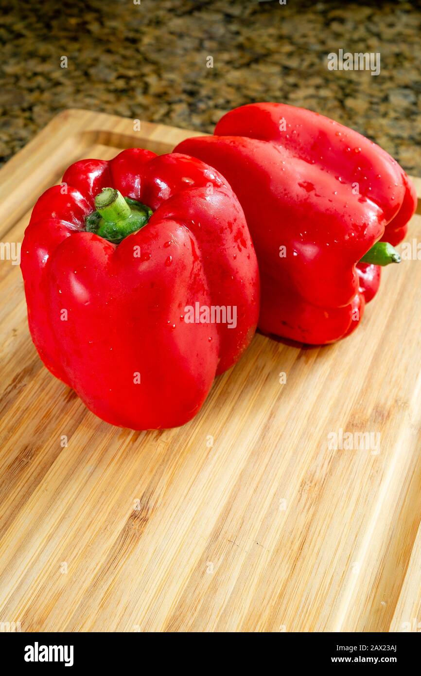 Peperoni rossi in un tagliere di legno, approccio realistico agli ingredienti alimentari imperfetti. Foto Stock