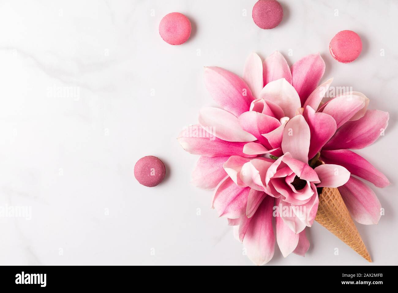 Fiori di magnolia rosa primavera in cono waffle con macaroons su sfondo bianco. Concetto di primavera. Piatto. Vista dall'alto. Vacanza sfondo festoso Foto Stock