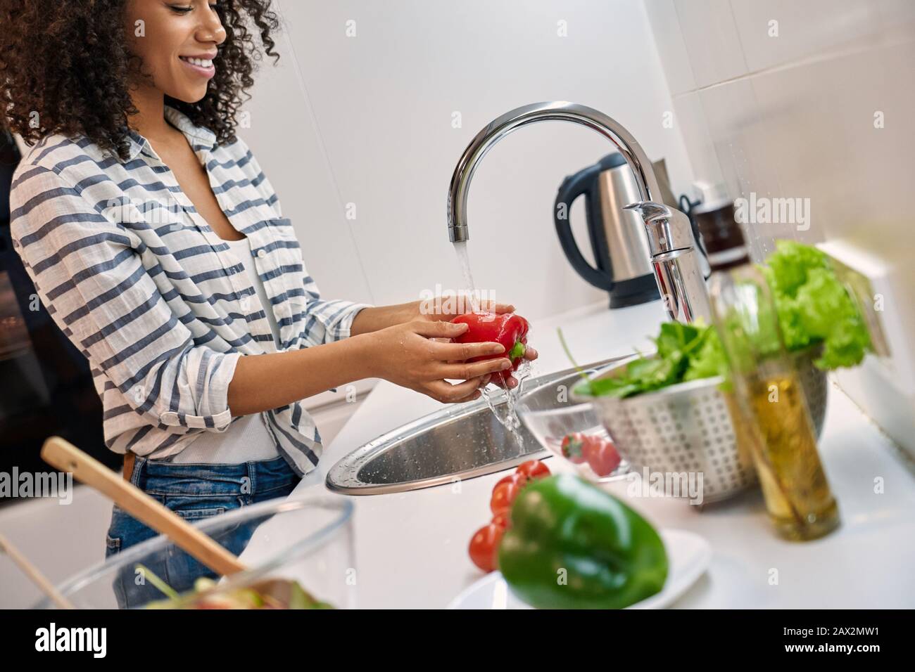 Dinenr. Sano Giovane donna africana in piedi in cucina a casa lavaggio verdure sorridente allegro primo piano Foto Stock
