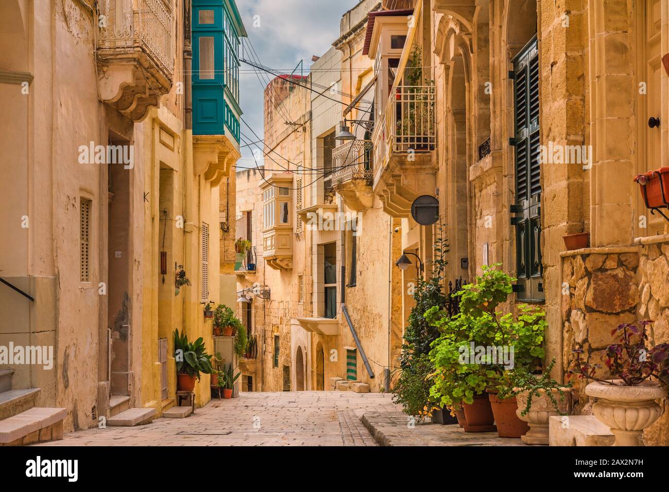 Vecchia strada medievale con edifici gialli, bei balconi e vasi di fiori a Birgu, Valletta, Malta senza nessuno Foto Stock