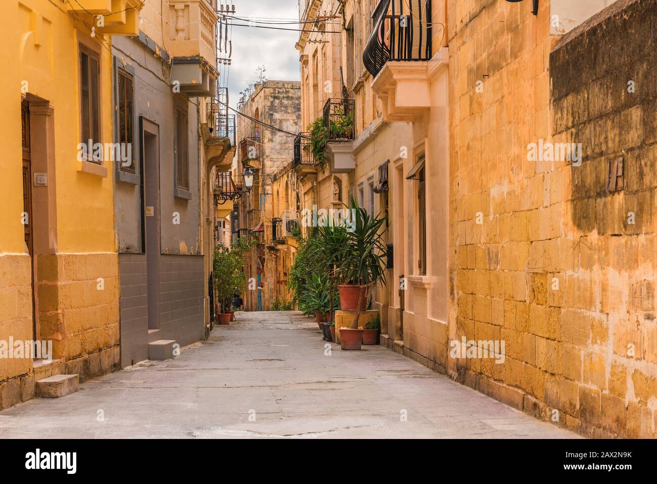 Vecchia strada medievale con edifici gialli e vasi di fiori a Birgu, Valletta, Malta senza nessuno Foto Stock