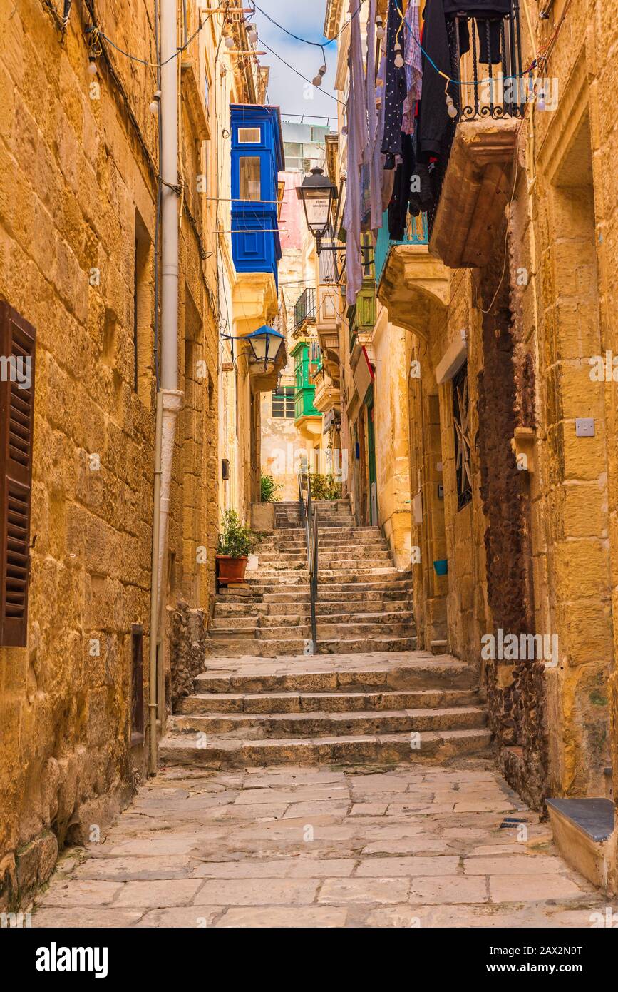 Vecchia e stretta strada medievale con edifici gialli con balconi colorati in città Singlea, Valletta, Malta senza nessuno. Orientamento verticale Foto Stock