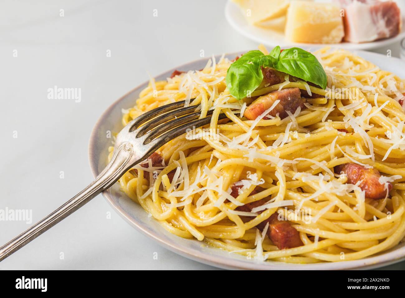 Pasta italiana carbonara a base di spaghetti, pancetta, parmigiano e basilico in un piatto con forchetta su tavolo in marmo bianco. Primo piano Foto Stock