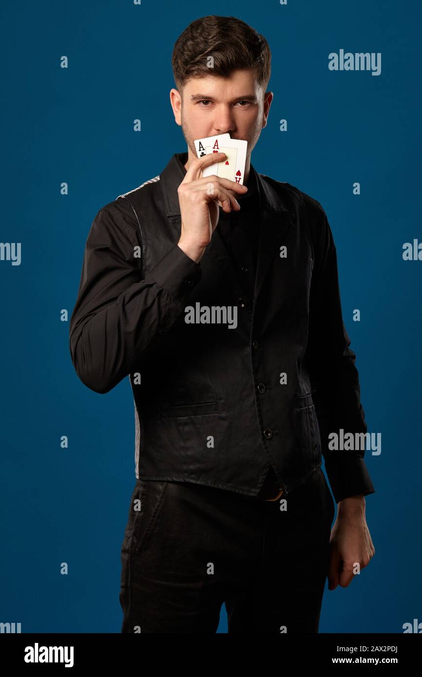 Elegante uomo, noob in poker, in gilet nero, pantaloni e camicia. Coprì la  bocca con due carte da gioco, assi, mentre si pose contro il backg blu  studio Foto stock - Alamy