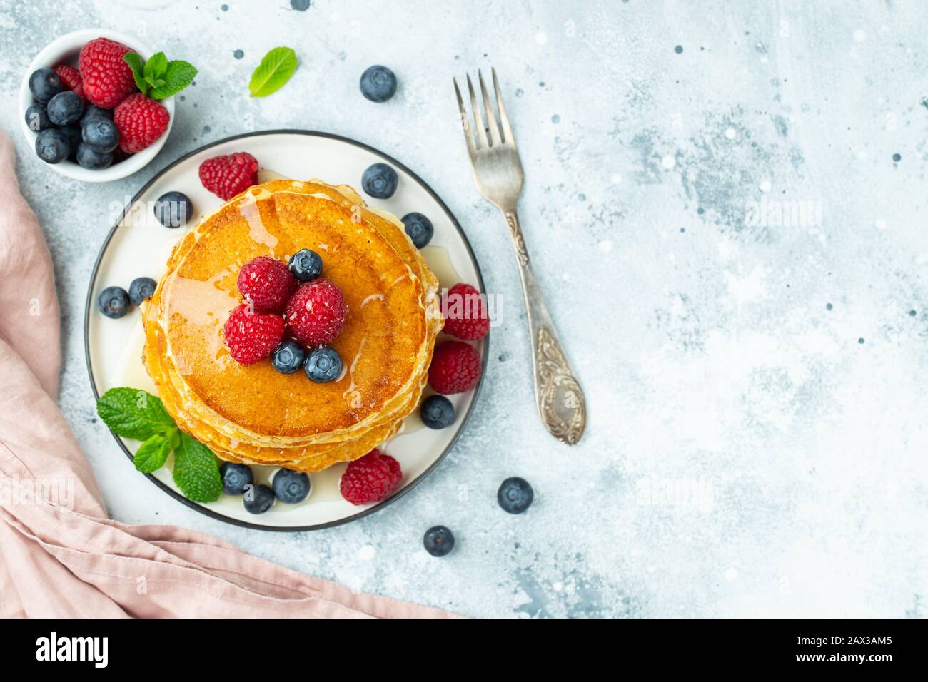 Primo piano deliziose frittelle dolci, con mirtilli freschi, lampone e miele su uno sfondo chiaro. Vista dall'alto con spazio di copia. Foto Stock