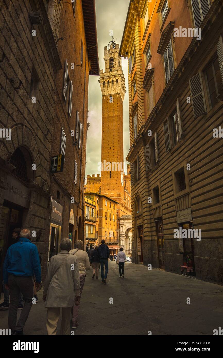 Palazzo del pubblico con la Torre del Mangia a Siena, Toscana, Italia con l'alta torre gotica che mostra alla fine dello stretto passaggio Foto Stock