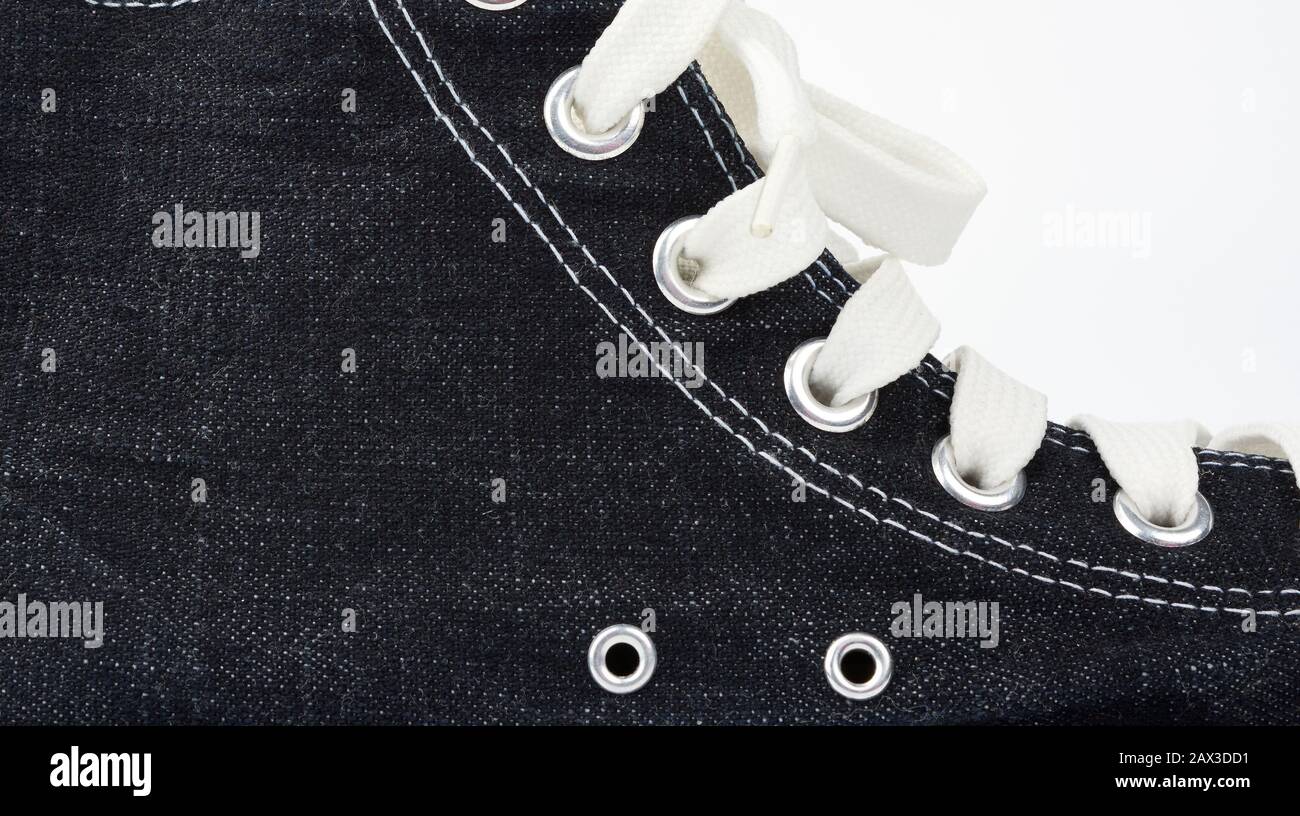 frammento di sneaker nera con lacci in tessuto bianco su sfondo bianco, primo piano Foto Stock