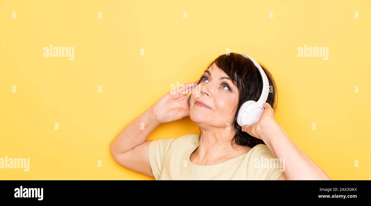 Bellissima donna anziana che balla e si rilassa con le cuffie wireless su sfondo giallo Foto Stock