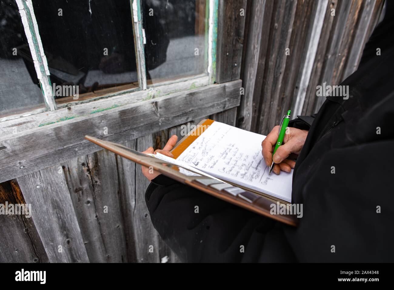 Ispettore domestico prendere appunti su un notebook durante un'ispezione. Primo piano sulle sue mani e sulla penna mentre esamina una finestra di una vecchia casa di legno Foto Stock