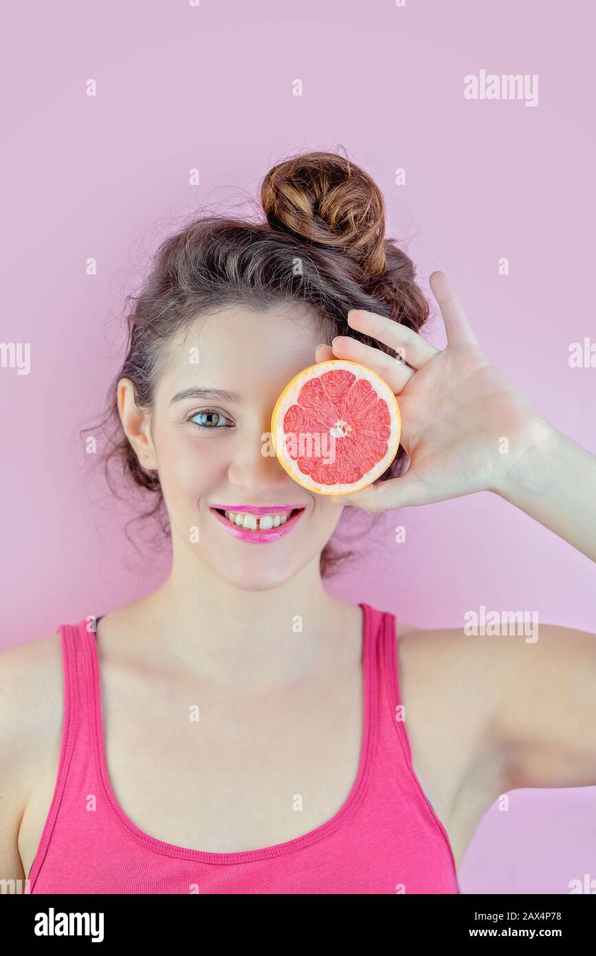 Bella brunetta in cima rosso mantiene arancione come un occhio su sfondo rosa, concetto di bellezza Foto Stock