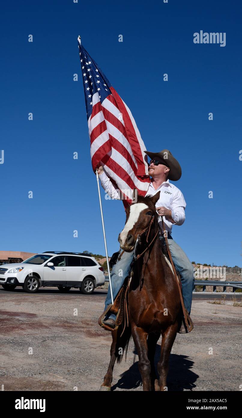 Un membro di un gruppo chiamato Cowboys per Trump, a cavallo, armato di una pistola e che porta una bandiera americana, partecipa a un rally pro-Trump. Foto Stock