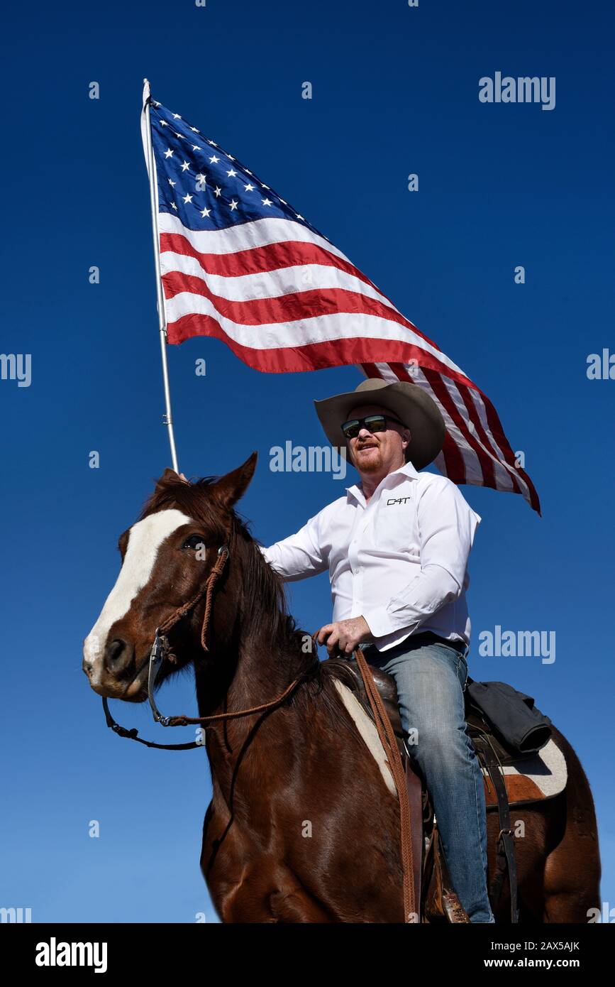 Un membro di un gruppo chiamato Cowboys per Trump, a cavallo, armato di una pistola e che porta una bandiera americana, partecipa a un rally pro-Trump. Foto Stock