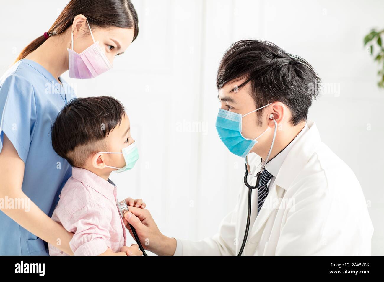 il medico indossa la maschera e sta esaminando il ragazzino in clinica Foto Stock