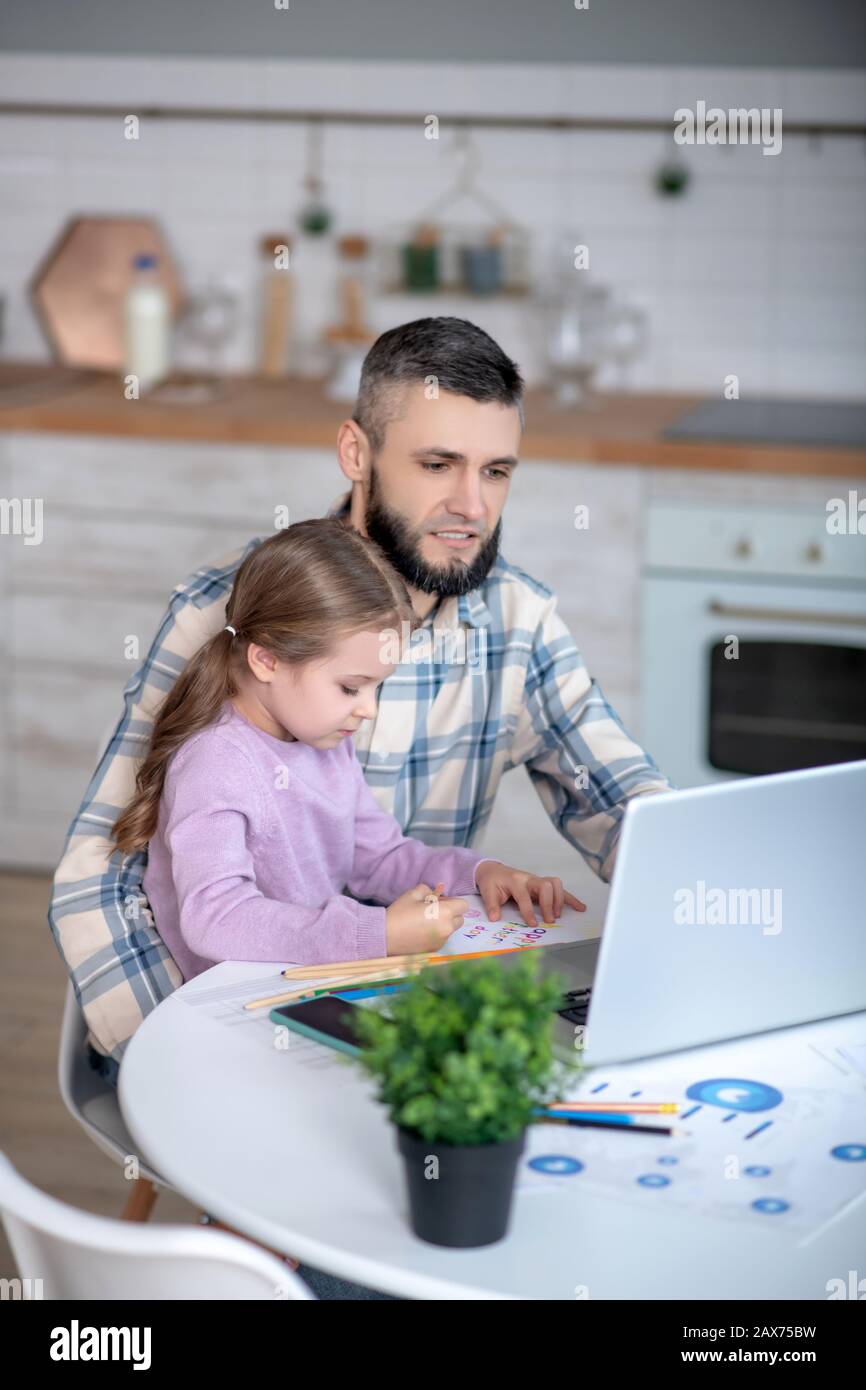 Giovane papà che lavora su un computer portatile, figlia seduta su mani di papà. Foto Stock