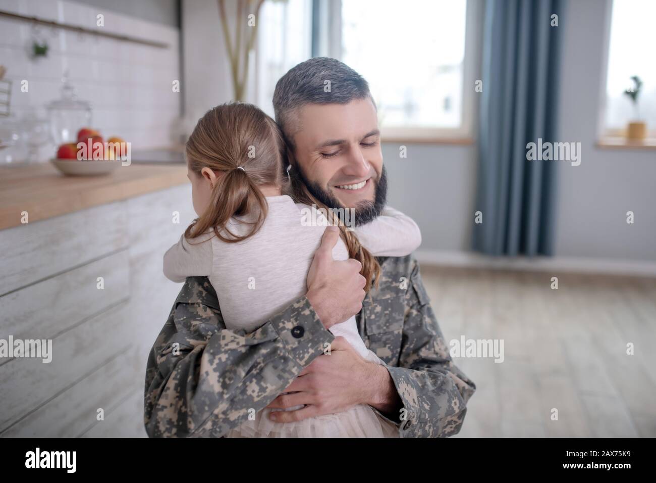 Papà sorridente in uniforme abbracciando strettamente figlia. Foto Stock