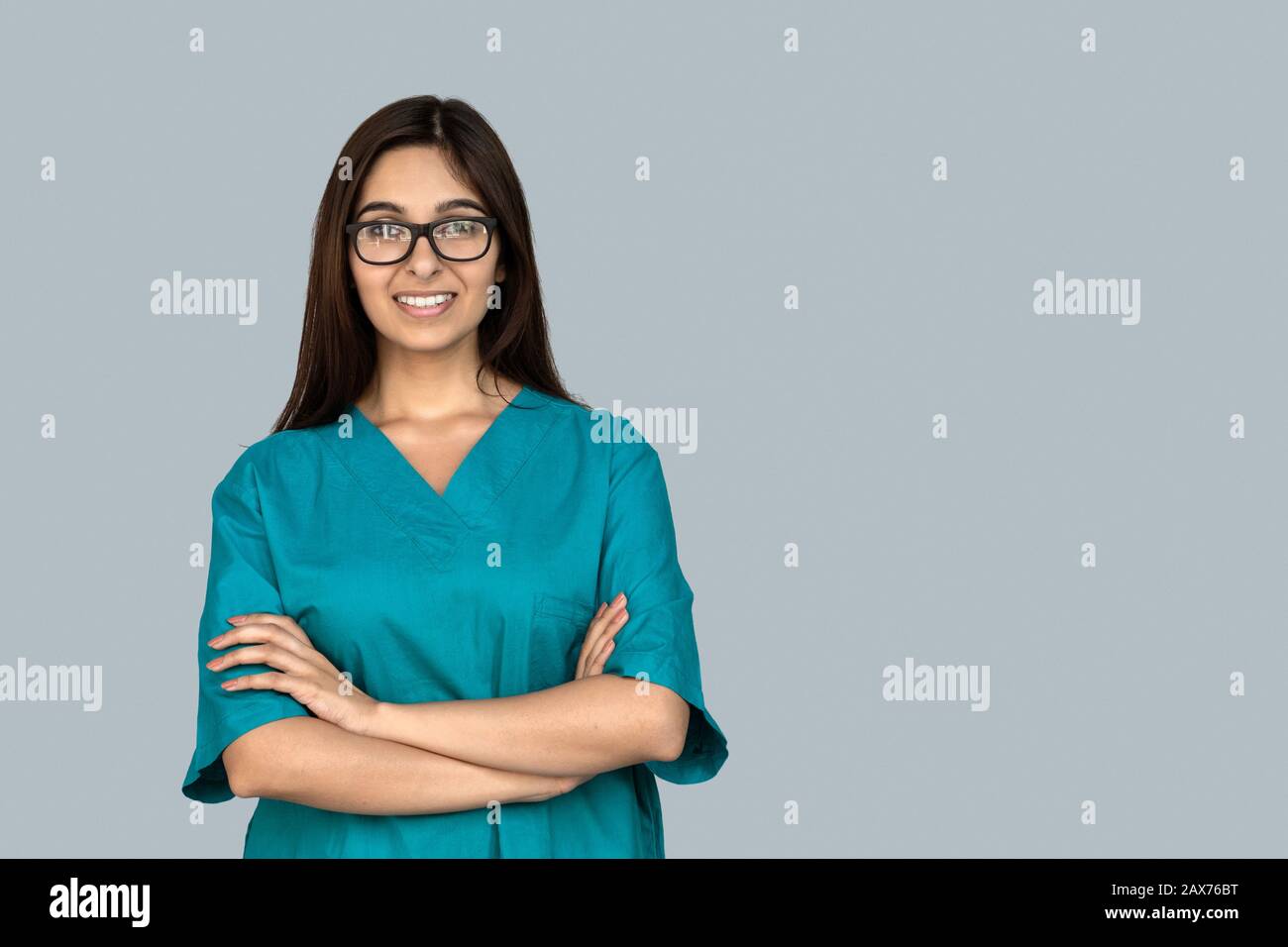 Sorridente giovane indiana donna infermiera braccia incrociate guardare la macchina fotografica isolato sul grigio Foto Stock