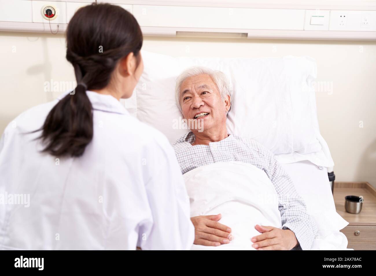 Giovani asiatici medico parlando a senior paziente al posto letto in hosptial ward Foto Stock
