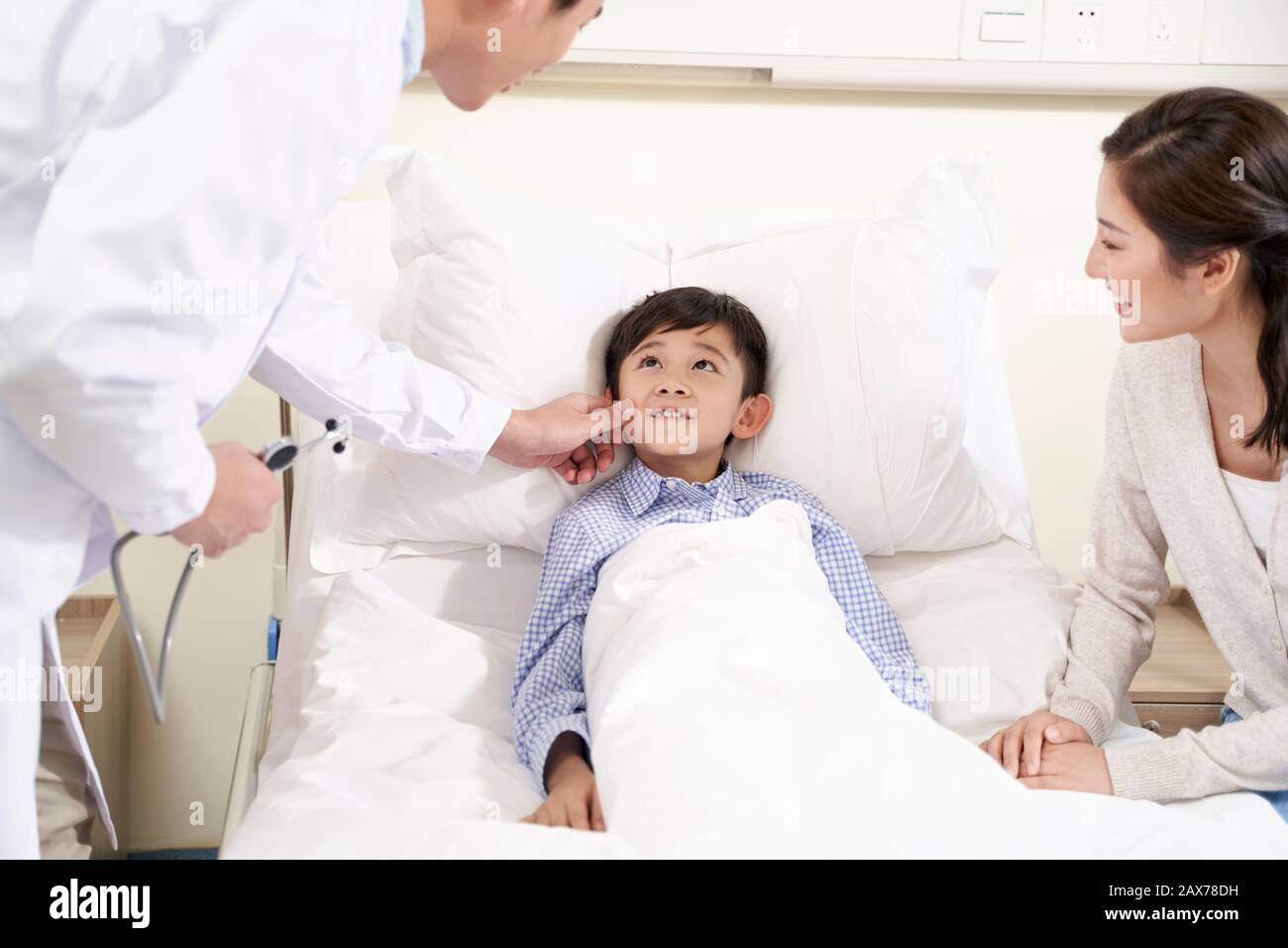 Cinque anni bambino asiatico che giace nel letto di ospedale accompagnato da madre a parlare con il medico Foto Stock