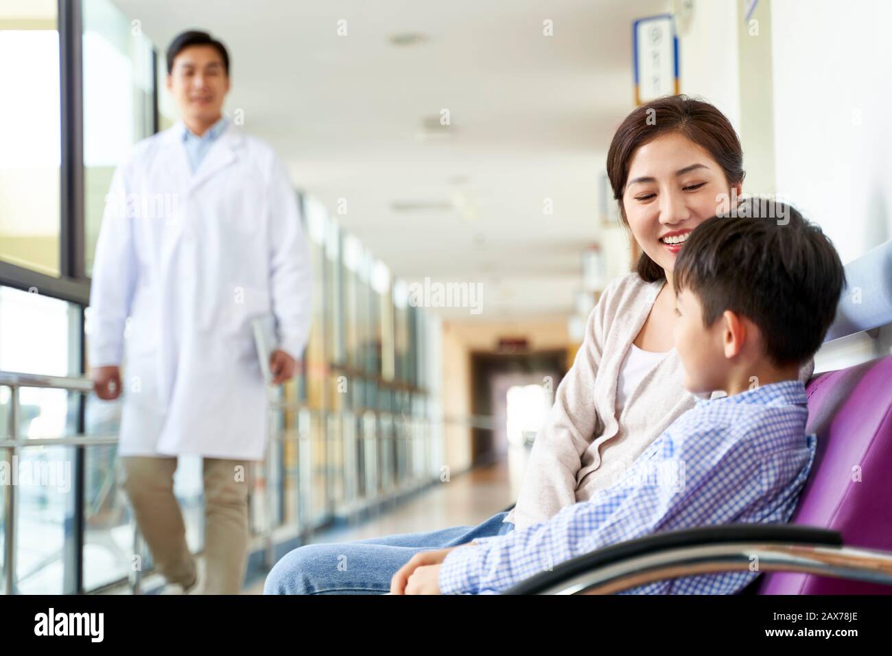 felice giovane madre asiatica e figlio seduto in sedie nel corridoio dell'ospedale Foto Stock