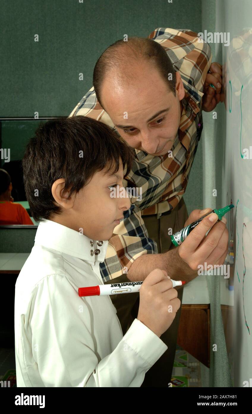 Insegnante arabo che insegna a un ragazzo come scrivere, Dammam Arabia Saudita. Foto Stock