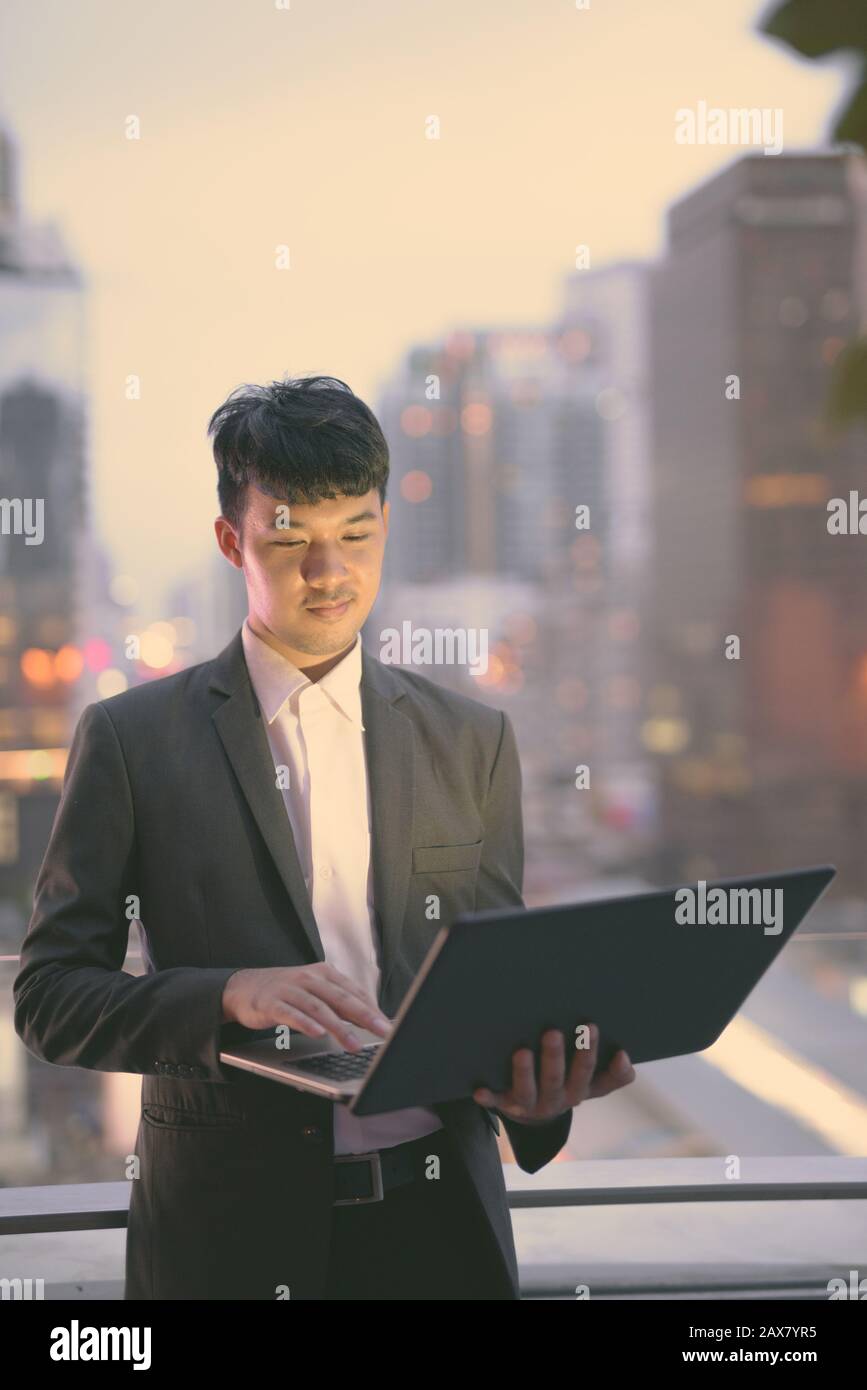 Giovane uomo d'affari asiatico contro la vista della città Foto Stock