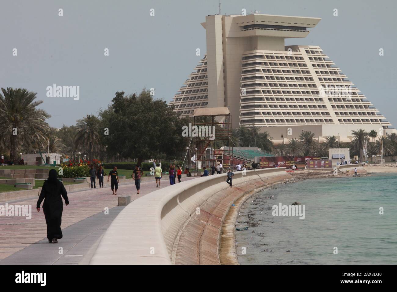 Una donna cammina lungo la Corniche a Doha con lo Sheraton Hotel in vista. Foto Stock