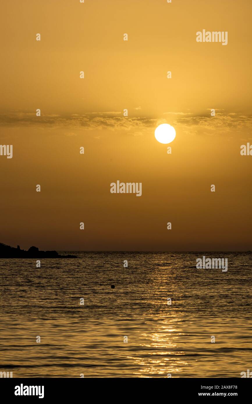 Focus sulla cornice rotonda Sun. Cerchio di sole sulla spiaggia al tramonto di fronte al Mar Ionio d'oro acqua con leggere nuvole overcast. Crepuscolo come visto da Ksamil, Albania, scenario di primavera sera. Foto Stock