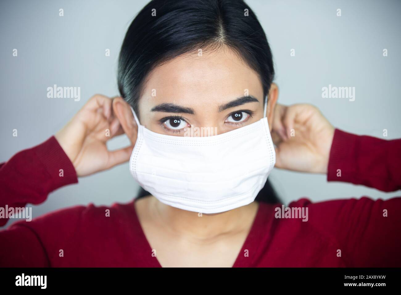 Una donna che mette su una maschera medica monouso per evitare virus contagiosi. Foto Stock