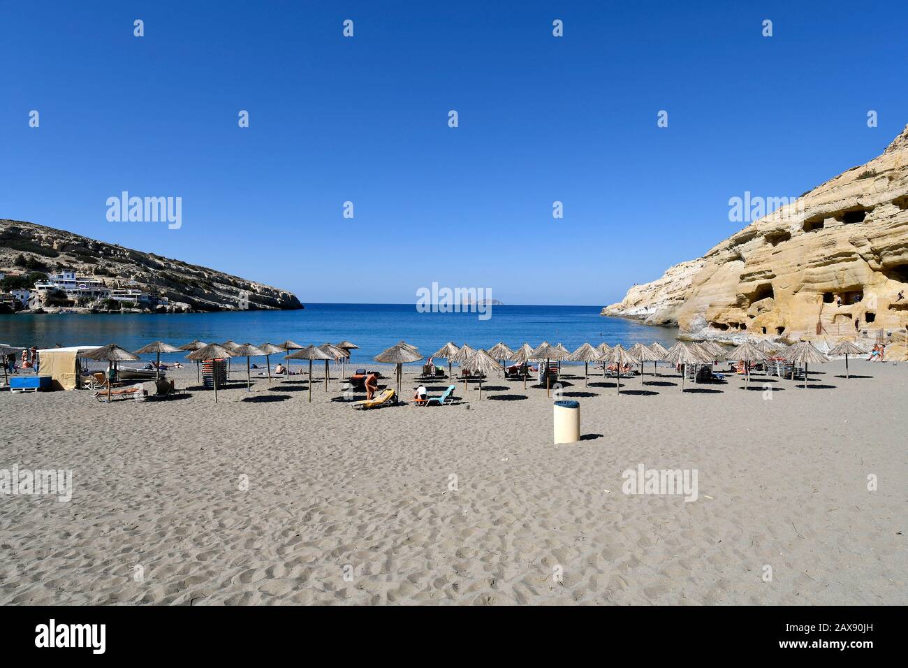 Matala, Grecia - 07 ottobre 2018: Persone non identificate sulla spiaggia sabbiosa con antiche tombe a destra e isole Paximadia sullo sfondo, Foto Stock