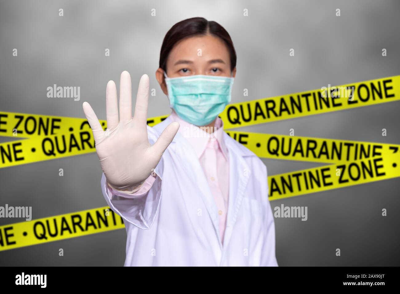 Il medico asiatico indossa una maschera medica, alza la mano per il segno di stop per non entrare nella zona di quarantena con il segno giallo di quarantena sul retro, l'entrata è Foto Stock