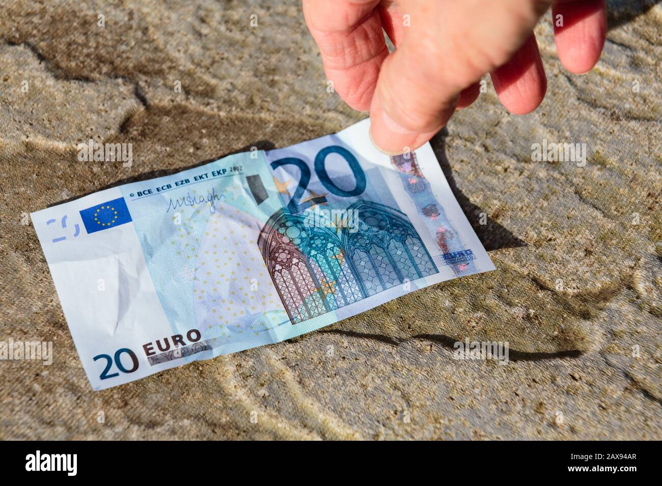 Una persona fortunata trova i soldi a terra una mano raggiunge giù per prendere una nota di venti Euro fuori dal pavimento. Europa Foto Stock