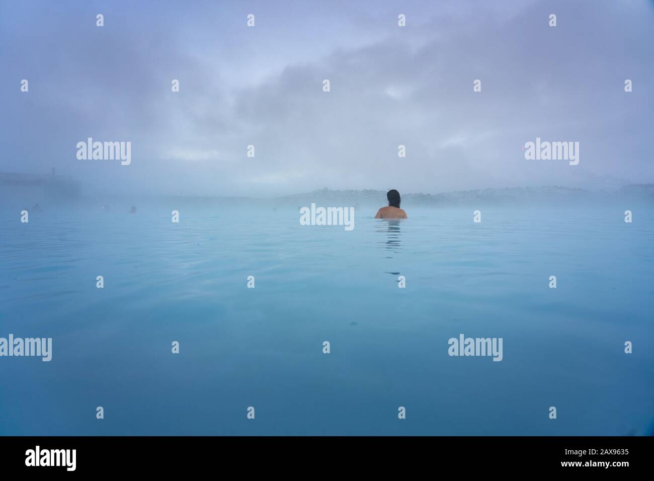 Donna che fa il bagno nella Laguna Blu vicino a Reykjavik con gente che fa il bagno in questa sorgente termale calda naturale Foto Stock