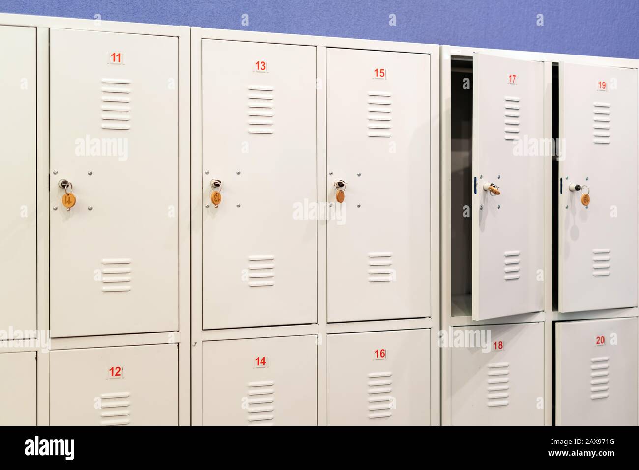 Una fila di armadietti scuola in metallo grigio con le chiavi nelle porte. Deposito ripostiglio in corridoio di istituto educativo Foto Stock