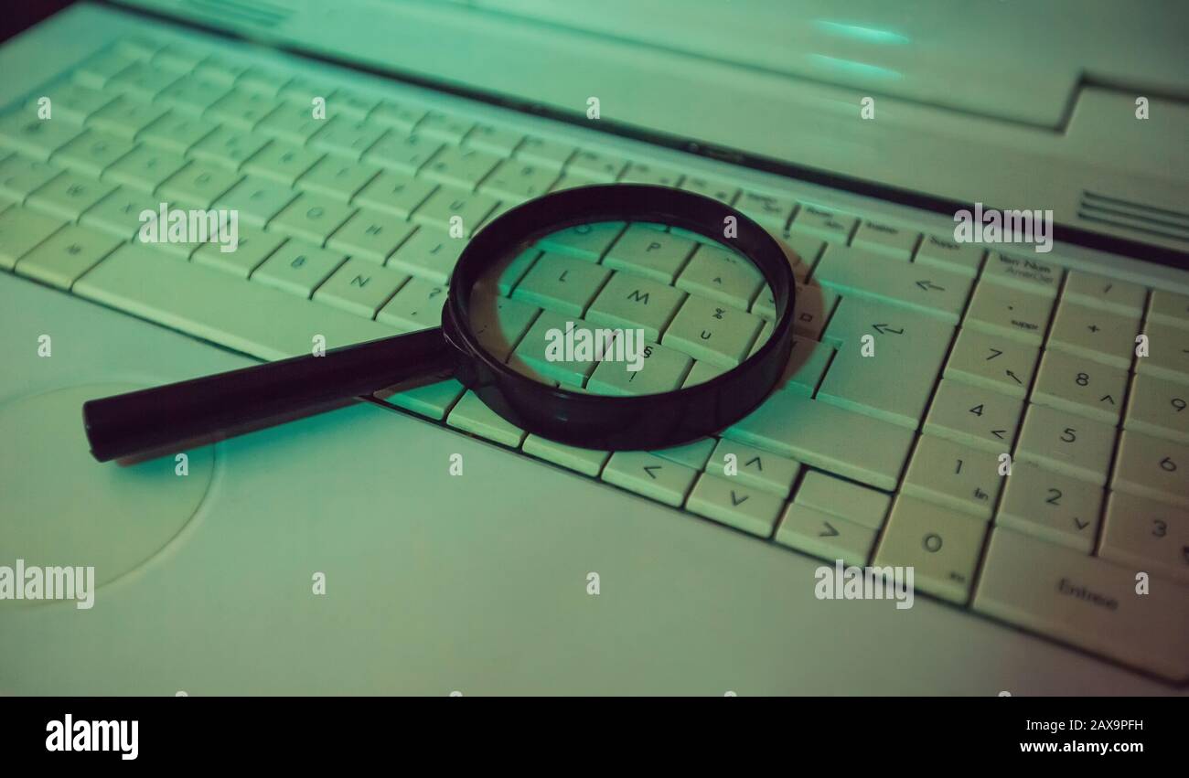 Primo piano di una lente d'ingrandimento su una vecchia tastiera del computer portatile. Motore di ricerca del calcolatore. Navigazione in rete per rispondere a ogni domanda. Trovare informazioni utili Foto Stock