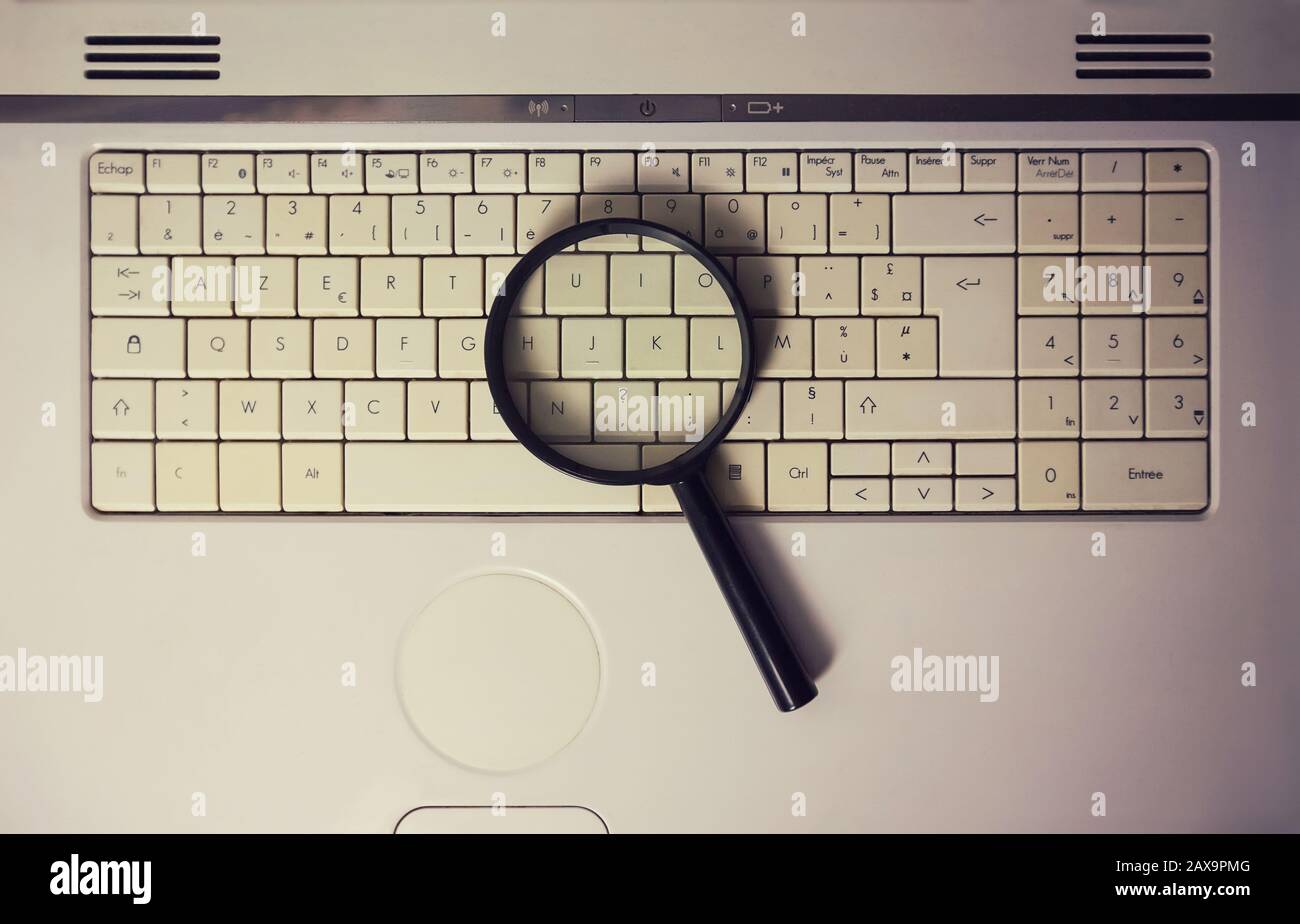 Primo piano di una lente d'ingrandimento su una vecchia tastiera del computer portatile. Motore di ricerca del calcolatore. Navigazione in rete per rispondere a ogni domanda. Trovare informazioni utili Foto Stock