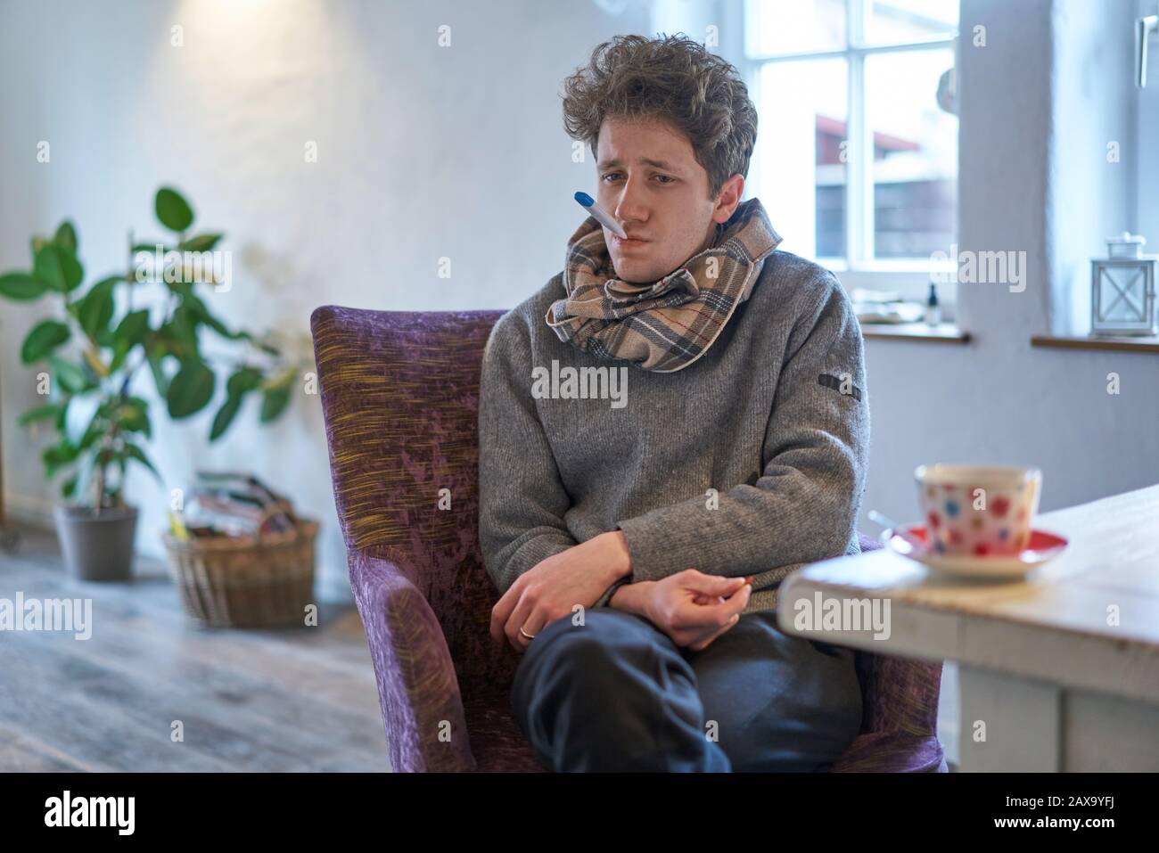 il giovane uomo si guarda stanco e esausto e ha un termometro in bocca perché ha appena misurato la sua temperatura non fa un viso incandescente Foto Stock