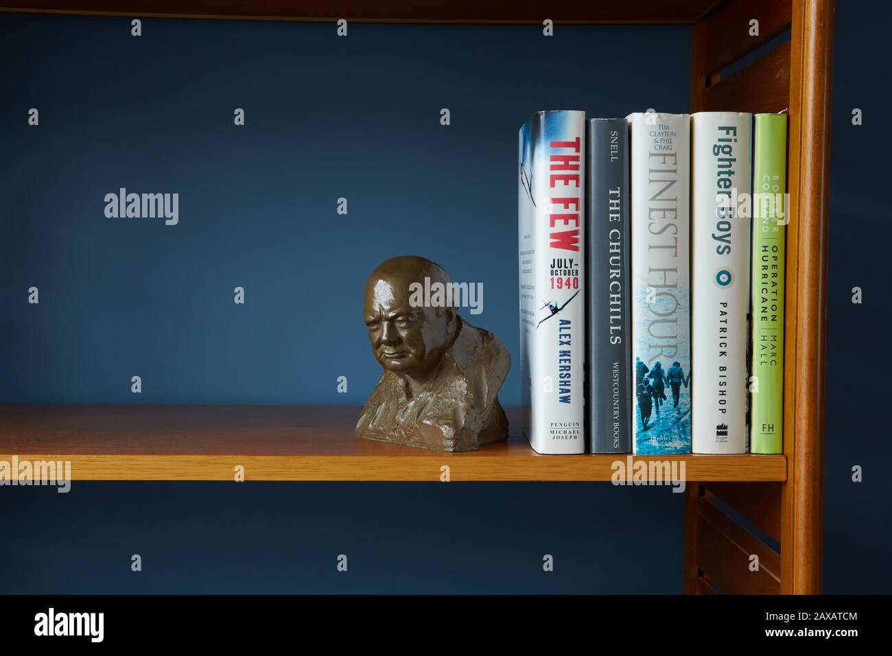 Un busto di Sir Winston Churchill messo su una mensola insieme con i libri circa la sua vita e La Seconda guerra mondiale. Su unità in teak con sfondo blu. Foto Stock
