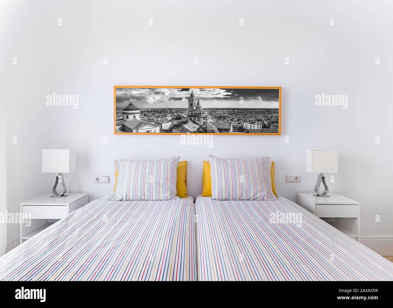 Camera da letto pulita e luminosa con letto, piumone, comodini, lampade, fotografia. Interni eleganti e minimalisti di colore bianco Foto Stock