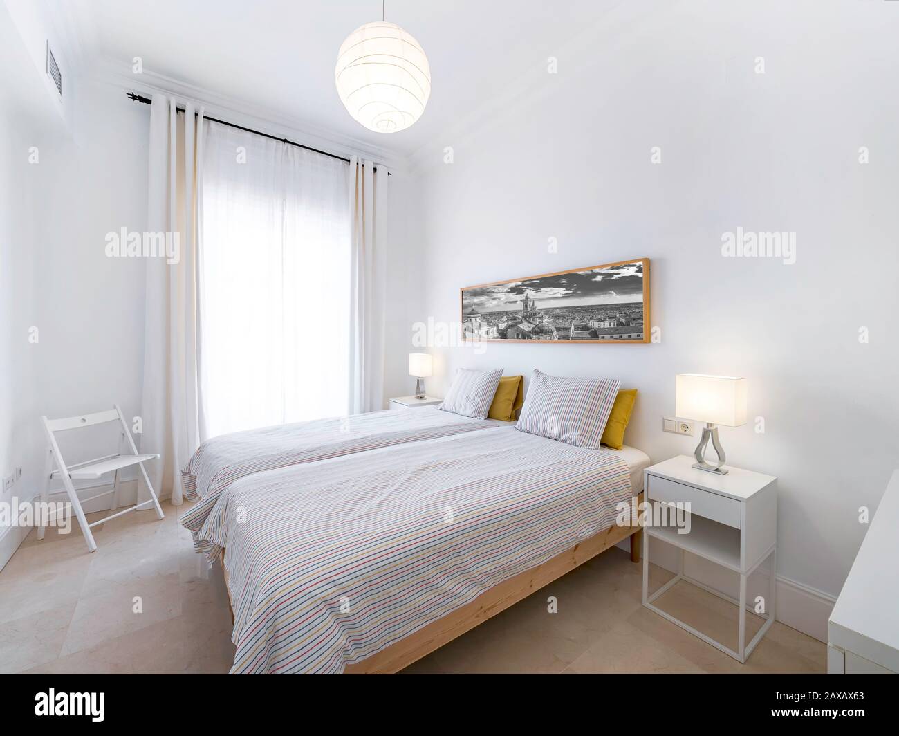 Camera da letto pulita e luminosa con letto, piumone, comodini, lampade, fotografia. Interni eleganti e minimalisti di colore bianco Foto Stock