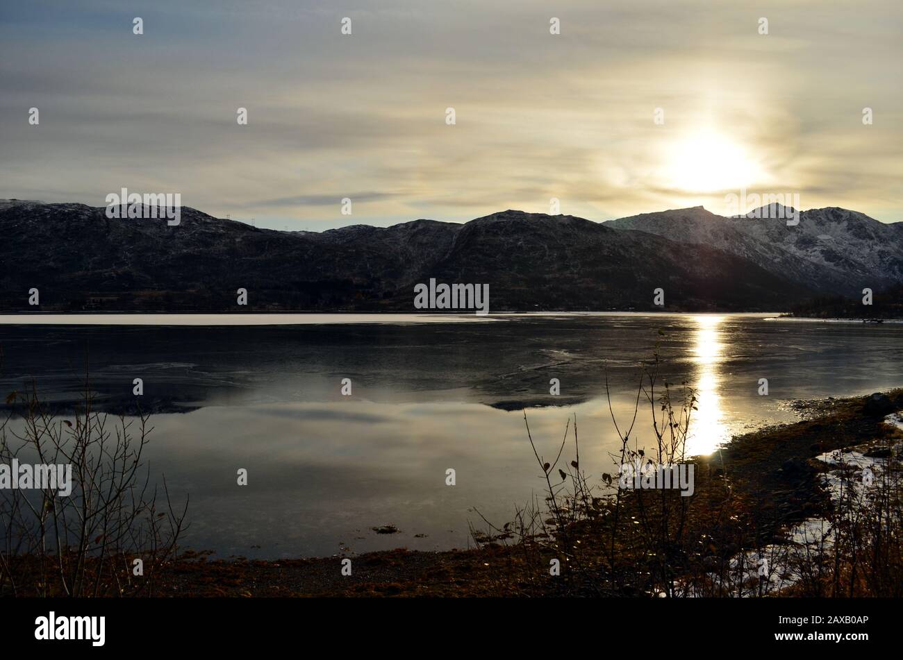 Lo scatto del sole che sta per prendere un riposo in nuvole dietro le montagne sulla riva del lago di montagna Foto Stock