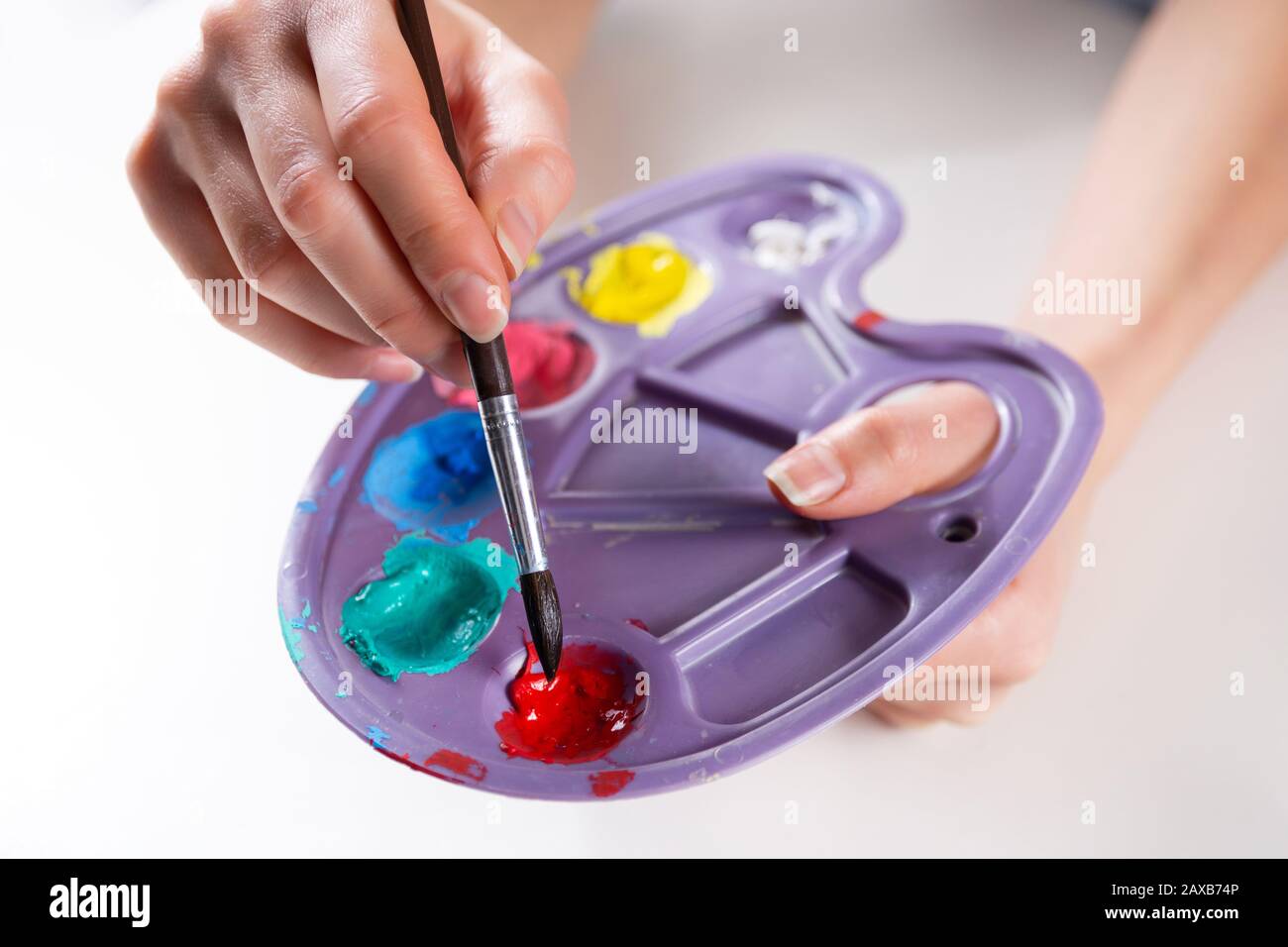 Pennello in femminile artista mani miscelazione vernici su una tavolozza. Ragazza che tiene tavolozza di plastica con vari colori e miscelazione. Arte e pittura concetto Foto Stock