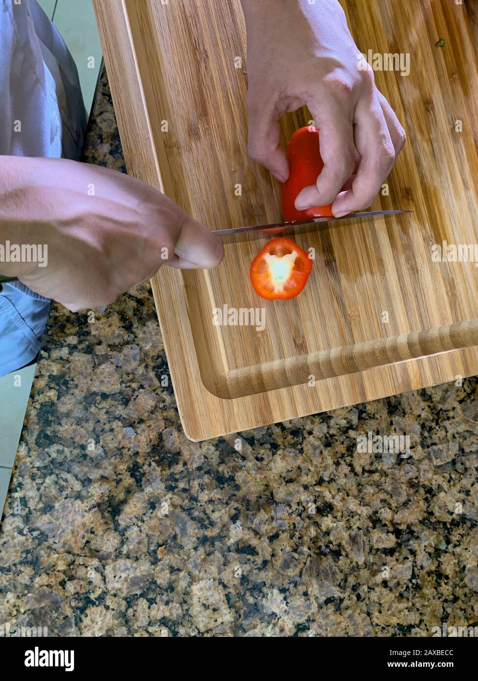 Lo chef adulto morde i peperoni rossi su un tavolo di legno. Foto Stock