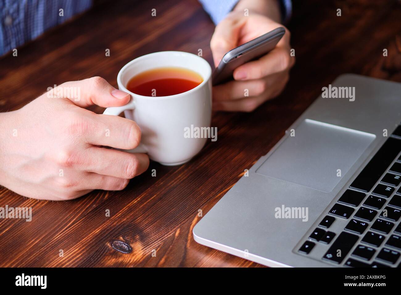 Il freelancer rilassa il tè bevente e naviga sui social network tramite il telefono accanto al suo laptop. Primo piano. Foto Stock